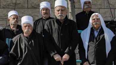 مجموعة من الرجال الدروز المسنين يرتدون الزي التقليدي الأسود والعمائم البيضاء يقفون أمام جدار حجري