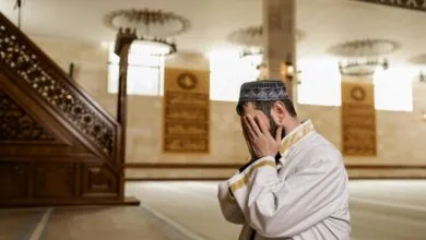 رجل مسلم يجلس في المسجد ويرفع يديه يغطي بهما وجهه في لحظة دعاء وخشوع قرب المنبر
