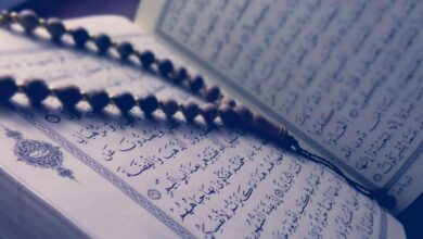 مصحف مفتوح مع مسبحة خشبية فوق صفحات القرآن الكريم، يظهر نص واضح من سورة التوبة، يمثل ارتباط الإسلام بالقرآن الكريم والعبادات الروحية.